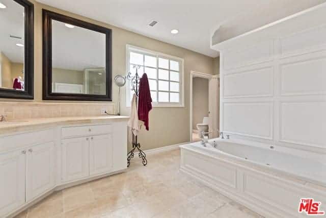 这个明亮的主浴室有米黄色的墙壁，白色的橱柜和白色的木结构容纳了浴缸。梳妆台旁边有一块漂亮的锻铁立式大衣地毯，用来放毛巾和长袍。