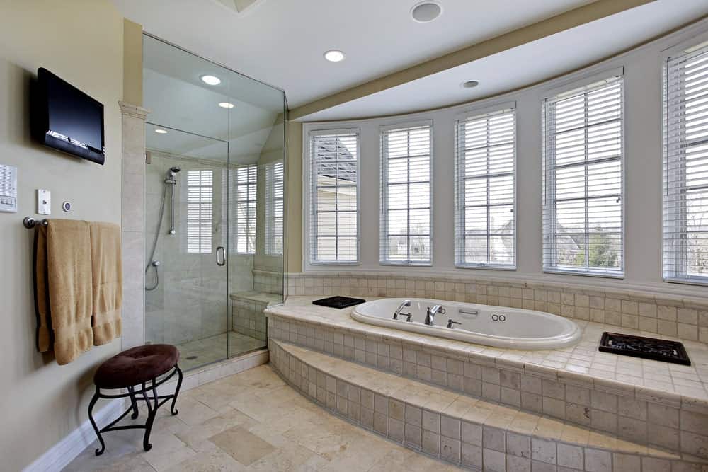 这个浴室的明亮品质是由于充足的自然光从浴缸上方的一排窗户中射入，浴缸外面包裹着与地板相同的米黄色瓷砖。