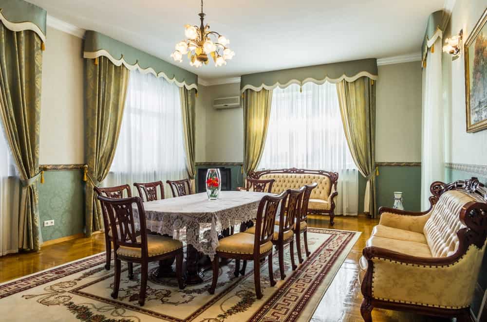 米色镶边地毯铺在丰富的硬木地板上，这间迷人的餐厅配有碎花玻璃吊灯和木制餐桌，配有软垫椅子和配套的沙发。