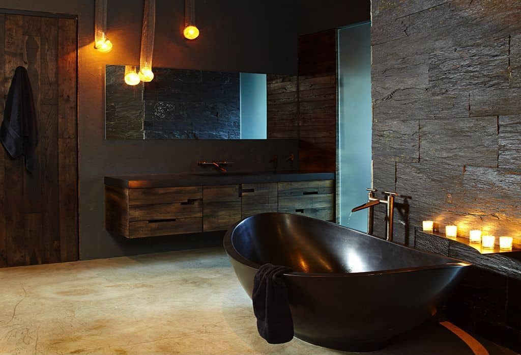 宽敞的主浴室，黑色墙壁与黑色独立式浴缸相匹配。还有一个质朴的浮动梳妆台，与质朴的浴室门相匹配。