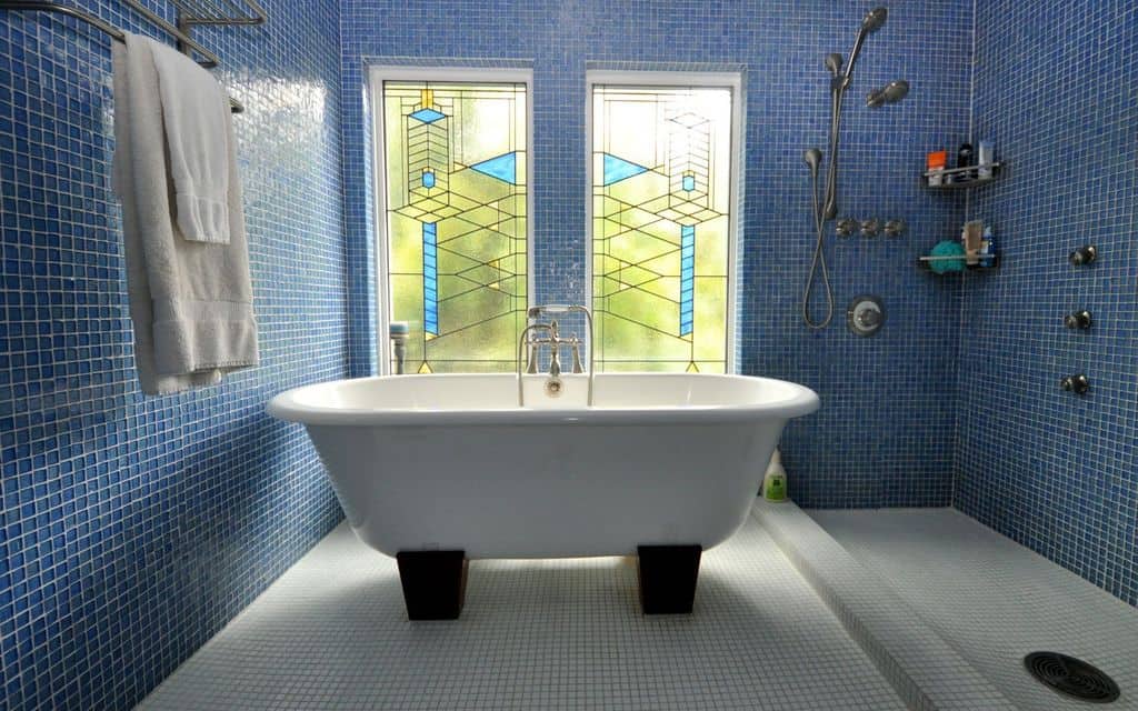 一间浅色的主浴室，拥有蓝色和白色瓷砖的墙壁和地板的组合。拐角处有一个很大的独立浴缸。