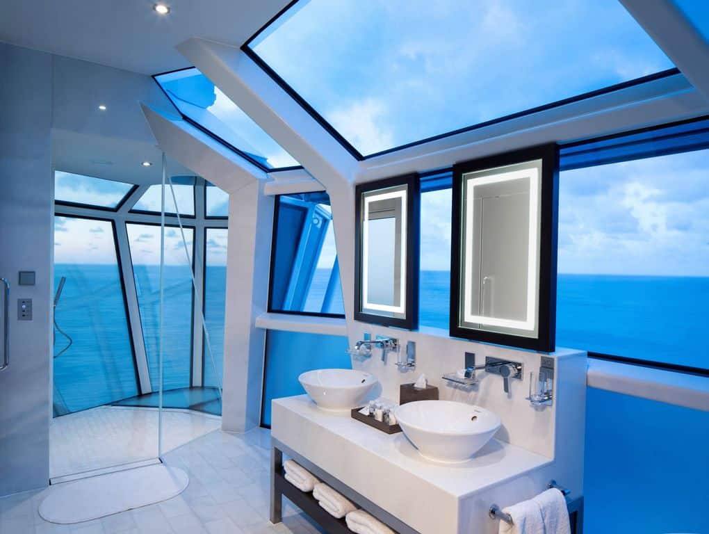 带有蓝色墙壁和多扇玻璃窗的当代主浴室可以俯瞰令人惊叹的海景。