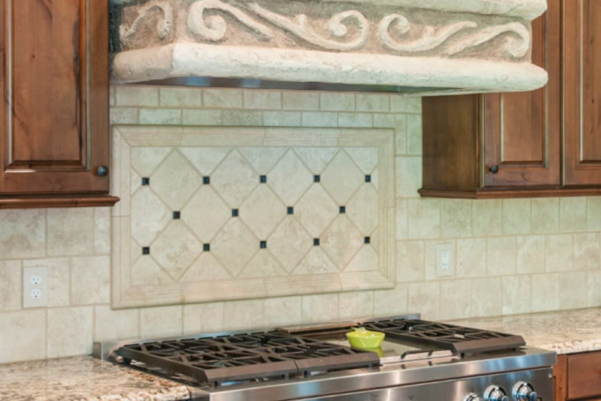 一个现代厨房，木柜上有美丽的细节，壁炉上方有一个镶框的焦点马赛克。