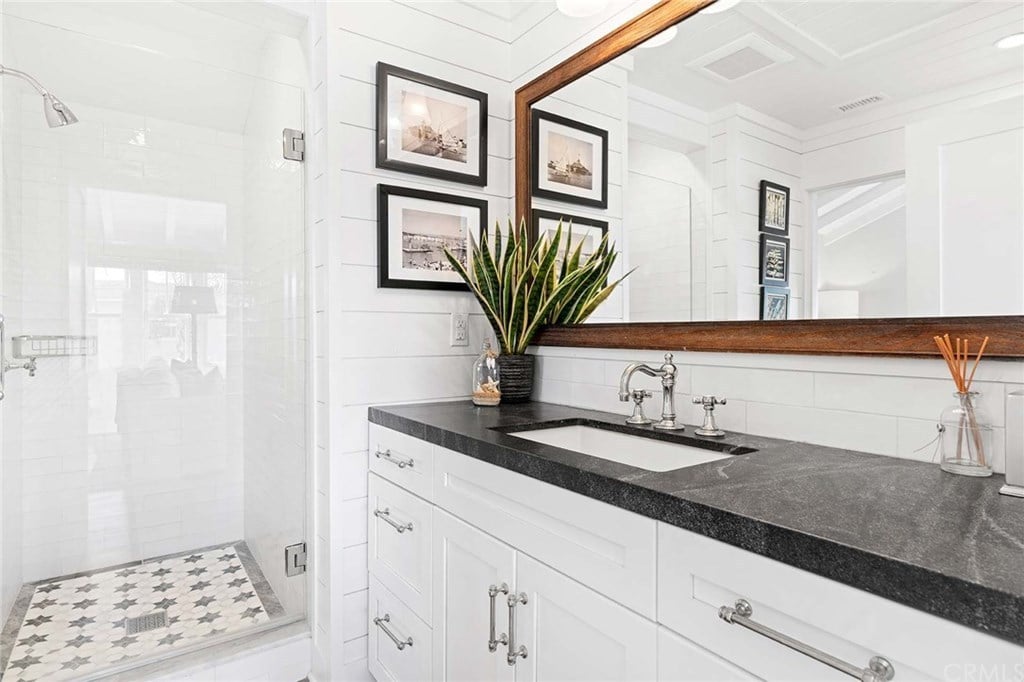 在这间小屋的浴室里，黑色花岗岩台面与白色的墙板和洗手台橱柜形成了鲜明的对比。这个房间里有一个步入式淋浴间，黑色的艺术品和一面长方形的镜子，在房间里创造了一个更大的视觉空间。