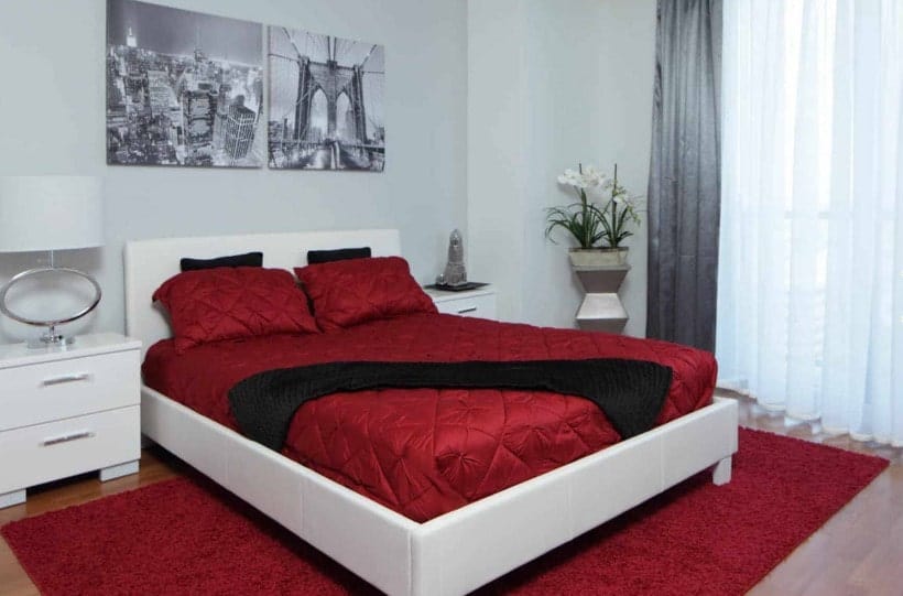 主卧室里有时髦的白色和红色的床，两个白色的床头柜和迷人的墙壁装饰。
