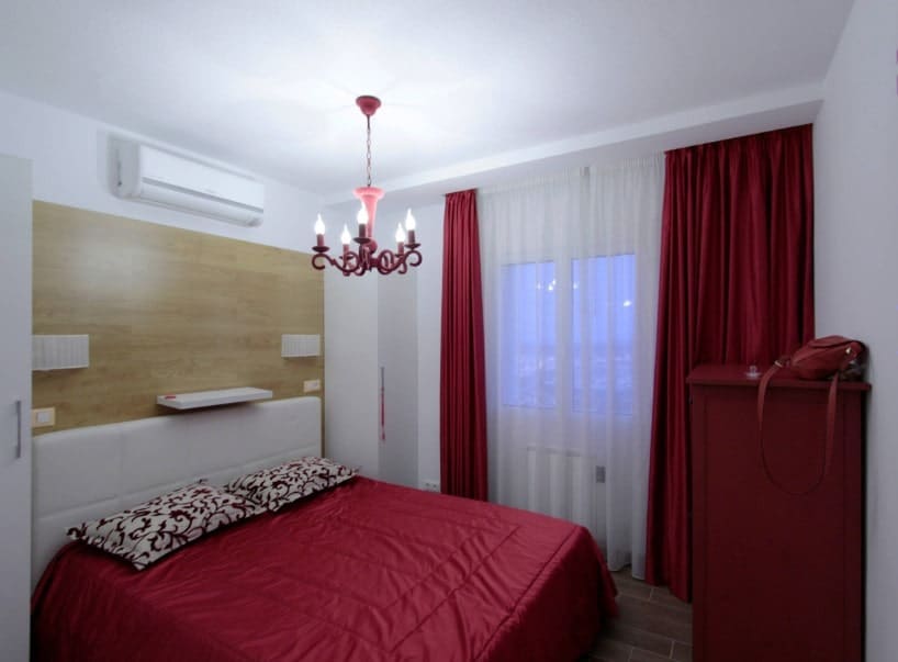 小主卧室设有红色舒适的床，红色橱柜和红色窗帘。房间里有一盏别致的枝形吊灯。