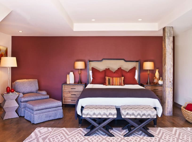 这间主卧室的特色是白色天花板和硬木地板，以及红色的墙壁。房间里有一张舒适的床，两侧床头柜上的台灯照亮了房间。