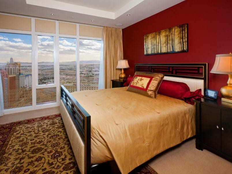 近距离观察这个主卧室的豪华床设置，两边都有优雅的台灯。房间里铺着地毯，上面铺着小地毯。还有一面红墙和一个托盘式天花板。