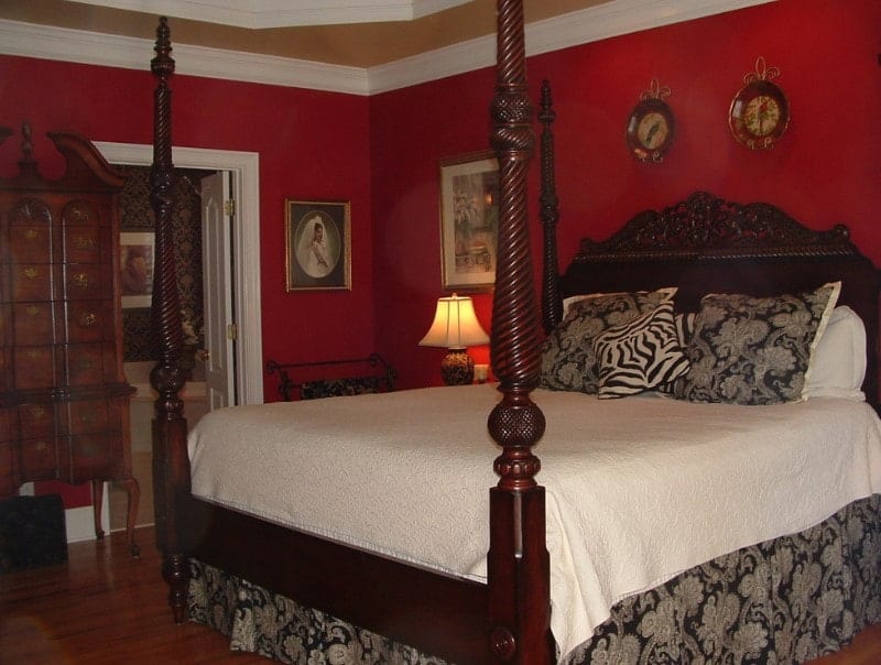 一个集中镜头在这个主卧室的经典的床设置周围的红墙和硬木地板。房间还提供自己的浴室，墙壁设计优雅。