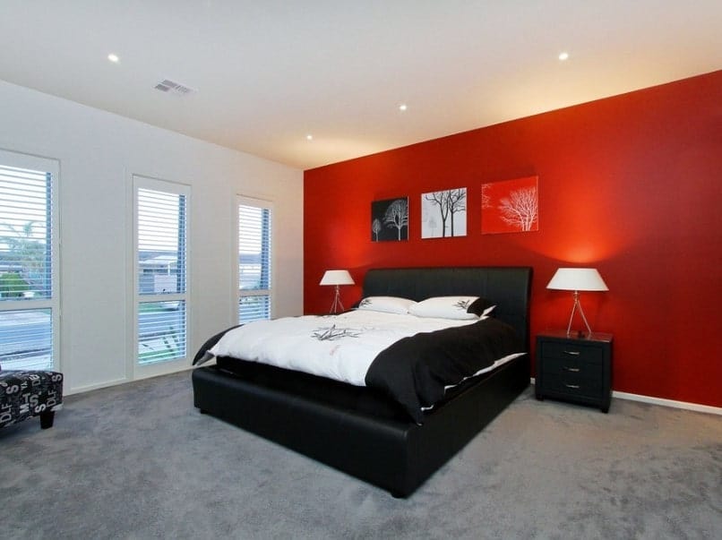 现代的主卧室以红色和白色的墙壁颜色组合为特色。它还有白色的天花板和灰色的地毯地板，以及黑色的床架。