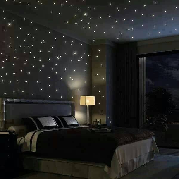 这间主卧室的特点是一张有裙摆的床和深色的木质床头柜，床头柜上有光滑的台灯。它由类似夜空中星星的嵌入式灯照亮。