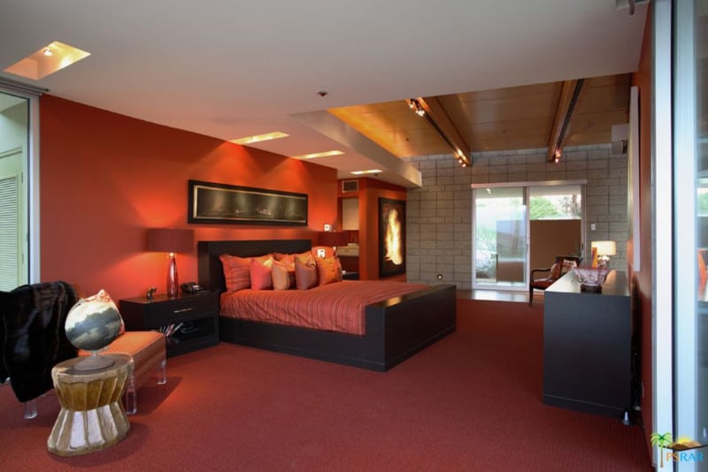 这间主卧室以墙壁、地毯地板和深色木框上的条纹床上用品的红色为主色调。它与白色天花板形成对比，天花板上安装了温暖的照明装置。