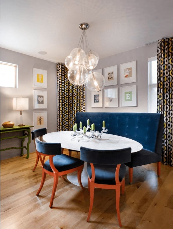 在这个当代风格的餐厅里，一串串玻璃吊坠悬挂在白色餐桌上，深蓝色的簇绒长凳和椅子靠在装有白色画廊框架的灰色墙壁上。