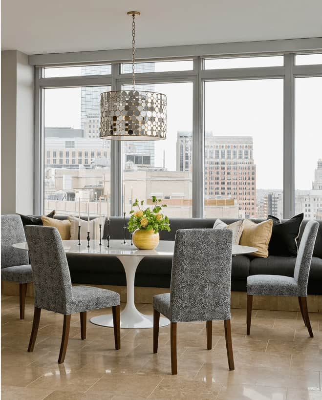 现代餐厅，大理石瓷砖地板和玻璃镶板窗户框架一个令人难以置信的城市景观。它有一张白色的餐桌，配有软垫椅子和内置的长凳，配有灰色靠垫。