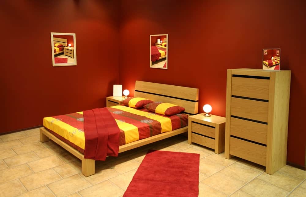 这个主卧室的床设置有配套的床头柜和橱柜，周围是红墙和瓷砖地板。