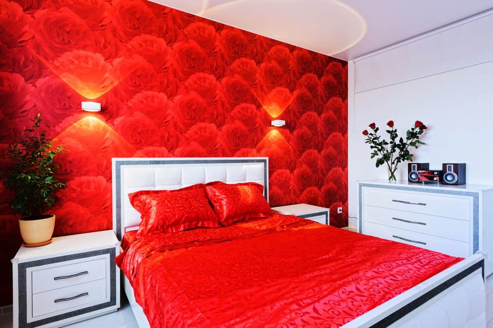 一个集中的镜头在这个主卧室的红色重音床设置与红玫瑰装饰的墙壁由壁灯照亮。