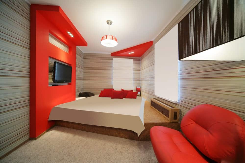 当代主卧室拥有一个定制的床设置，侧面有一个时尚的红色沙发，前面有一台宽屏电视机。