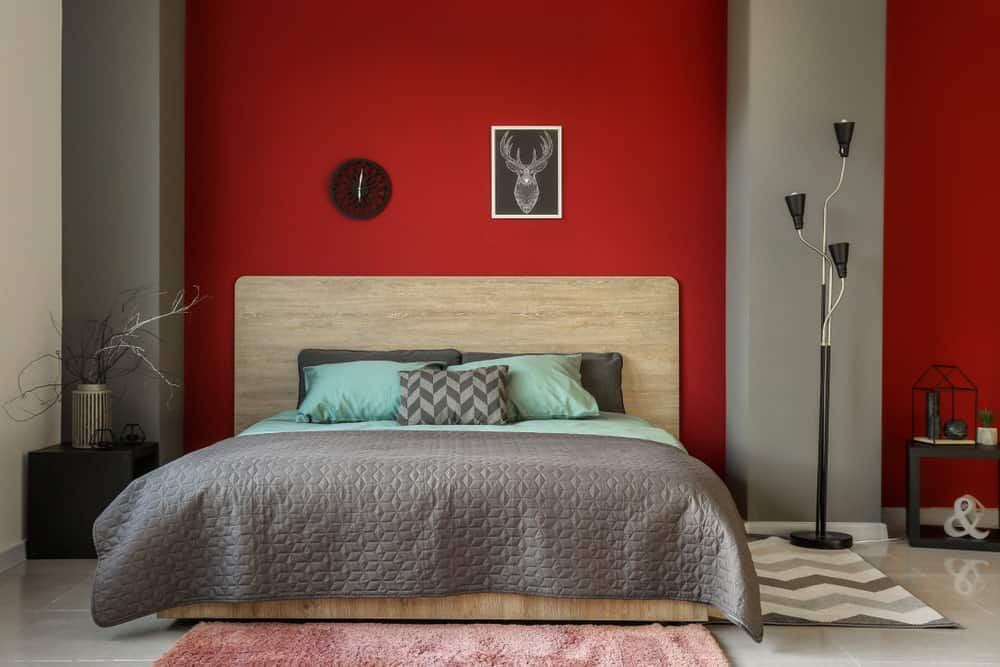 这张照片聚焦在这间主卧室的时髦床上，周围是灰色和红色的墙壁，看起来很美。