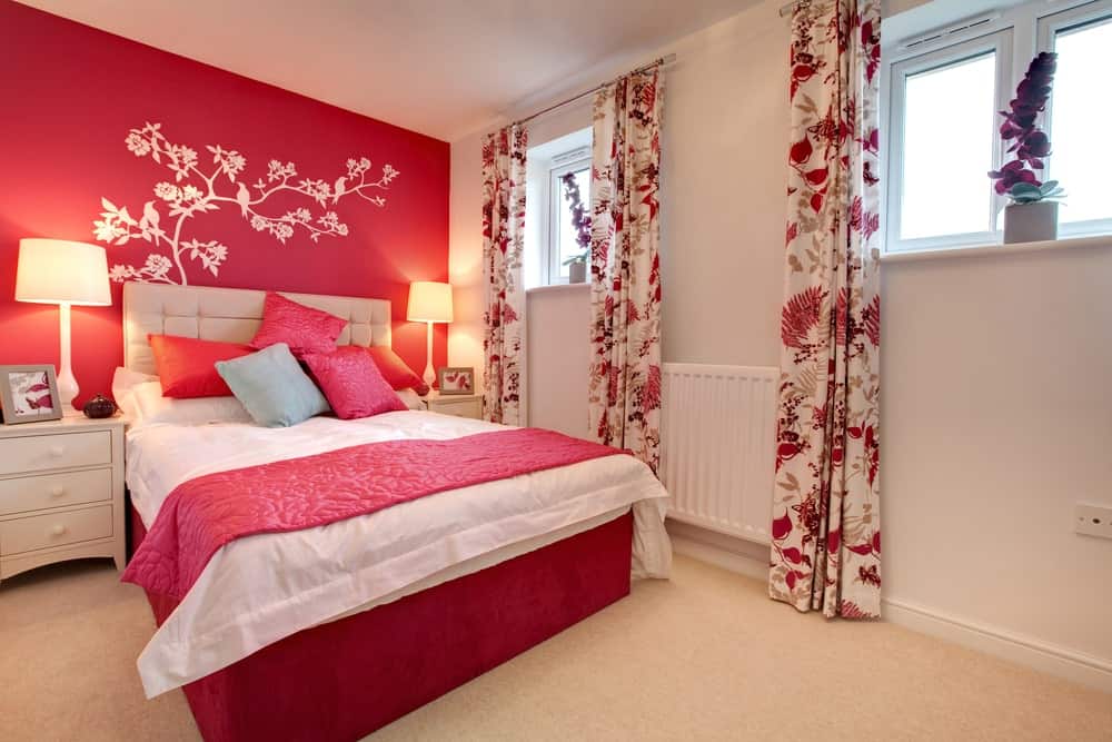 主卧室有一面红色的墙，装饰着可爱的红色口音窗帘和由台灯照亮的床上设置。