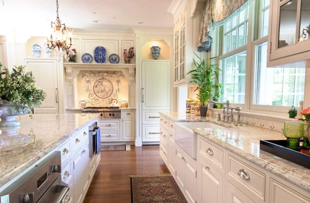 陶瓷盘子和花瓶为厨房里的白色橱柜增添了华丽的色彩，厨房里有玻璃窗和硬木地板，上面铺着经典的流苏地毯。它包括花岗岩台面和一个配有铬固定装置的农舍水槽。