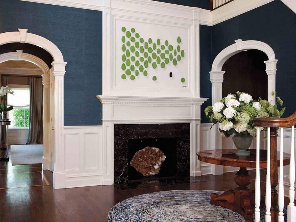 现代风格的门厅里有一座壁炉，位于深蓝色拱形墙壁中间，有白色护壁板，中间有一张放在圆形地毯上的木制餐桌。
