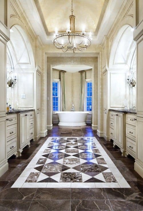 这个优雅的主要浴室设有一个迷人的瓷砖地板，由美丽的枝形吊灯照亮。走廊通向窗户附近角落的独立浴缸。