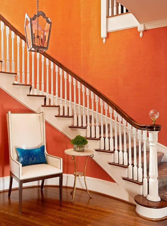 这个门厅以橙色的墙壁为特色，白色的细节与楼梯旁的椅子相匹配。