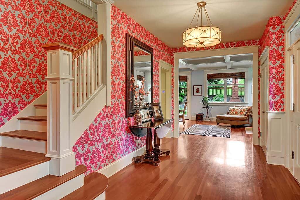 华丽的门厅，粉红色图案的壁纸和硬木地板。它有一个丰富的木控制台与一个巨大的镜子，并由一个鼓吊坠照明。