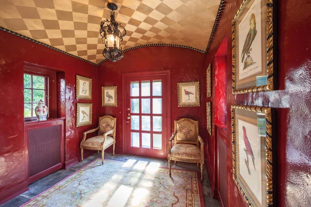 红色门厅设有一个经典的地毯和桶拱顶天花板。两个角落的椅子与墙壁装饰的框架相匹配。