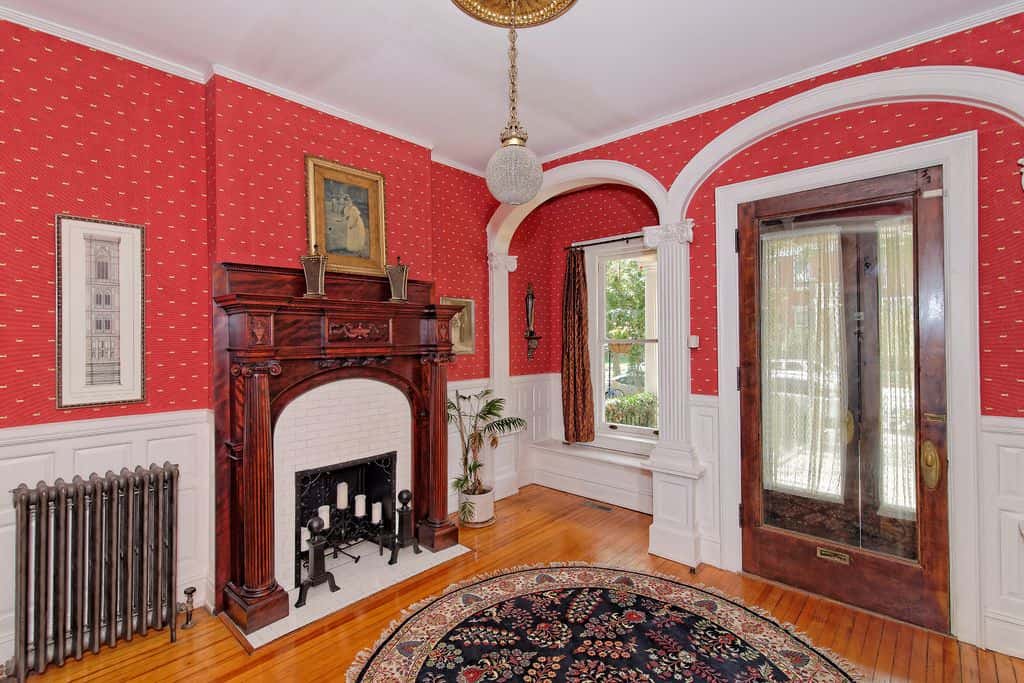 迷人的入口拥有红色墙纸上面的白色护壁板。它有一个木制的前门和窗户座位角落框与弯曲的皇冠造型。