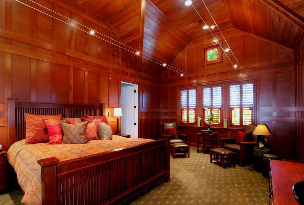 这间主卧室提供了一个舒适的休息区和一张与木镶板墙壁融为一体的木床。它有绿色的地毯地板和一个高高的教堂天花板，上面覆盖着木板。