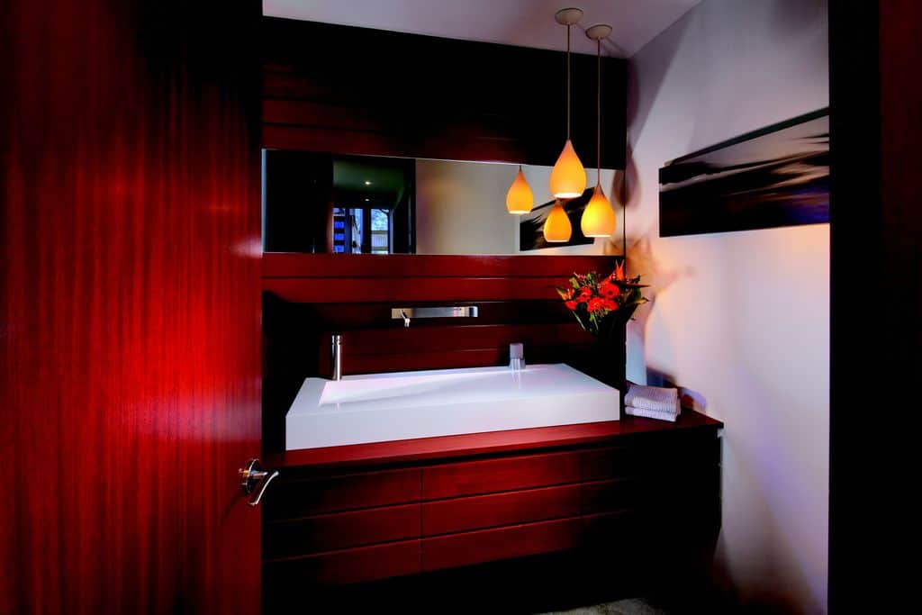 当代风格的浴室展示了一扇红木门，与顶部带有光滑水槽的浮动梳妆台相匹配。