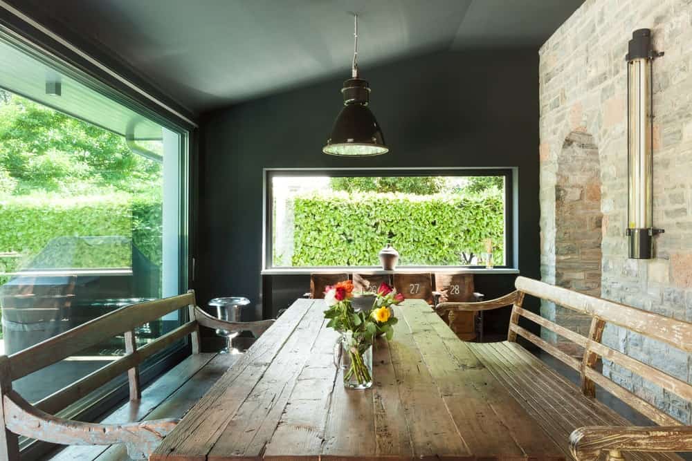 这张质朴的木制餐桌和配套的长椅搭配着光滑的黑色棚顶和黑色墙壁，砖墙上有一扇巨大的玻璃窗。