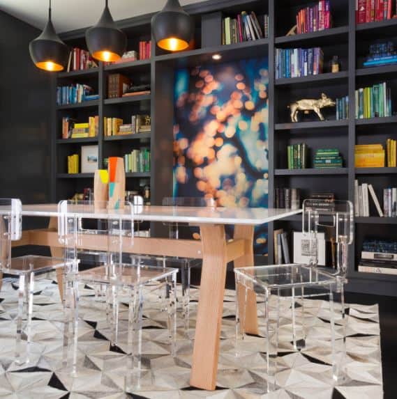 现代塑料椅子与白色的餐桌相搭配，餐桌与黑色书架形成鲜明的对比，黑色书架占据了墙壁，餐桌顶部有三盏黑色圆顶吊灯。
