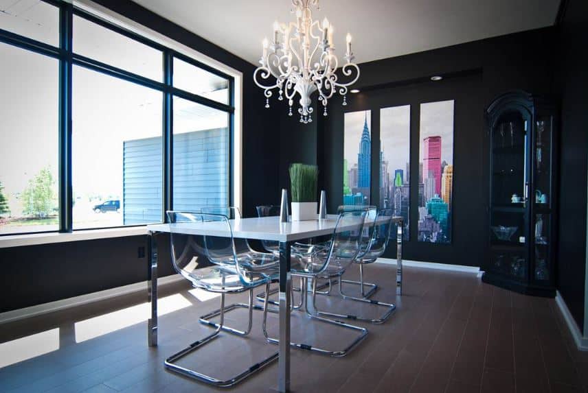 配有金属桌腿的现代塑料和白色餐台搭配着一盏复杂的白色枝形吊灯，与黑色的墙壁形成对比。