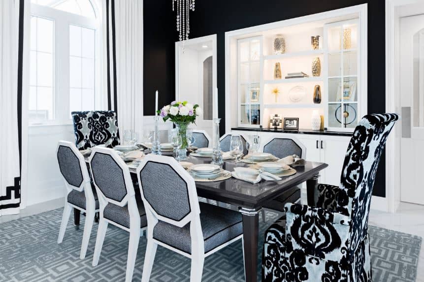 这是一个明亮的餐厅，白色和黑色元素的微妙平衡。黑色的墙壁与高大的窗户相搭配，餐桌上有几把带有黑色花卉图案的扶手椅。