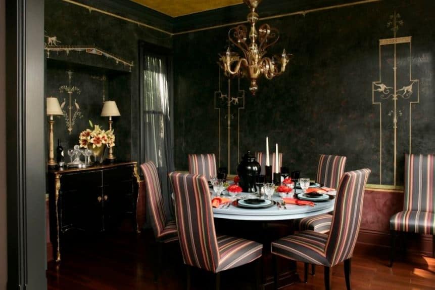 白色圆桌周围摆放着彩色条纹的帕森斯椅子，与餐厅的黑色墙壁形成鲜明的对比，餐厅顶部有一盏优雅的金色吊灯，与墙壁的金色细节相匹配。