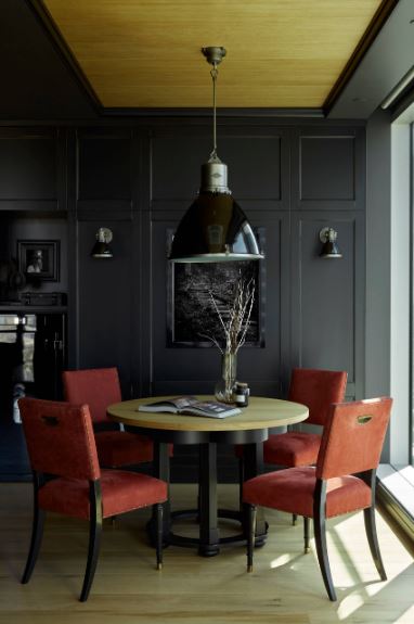 红色软垫餐椅环绕的木制圆桌在黑色墙壁和黑色托盘天花板的映衬下显得格外突出，木质托盘中心支撑着一个巨大的黑色圆顶吊灯。