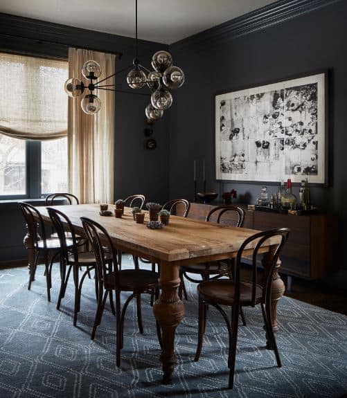 黑色的墙壁与墙上的艺术作品相呼应，在黑色的背景下显得格外突出。木制桌下的蓝色图案地毯与木椅相辅相成。