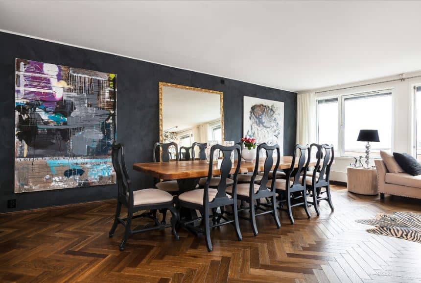 硬木地板与餐桌的木质顶部相匹配，餐桌周围环绕着优雅的深灰色椅子，这些椅子反过来与黑色的墙壁形成了巨大的艺术品。