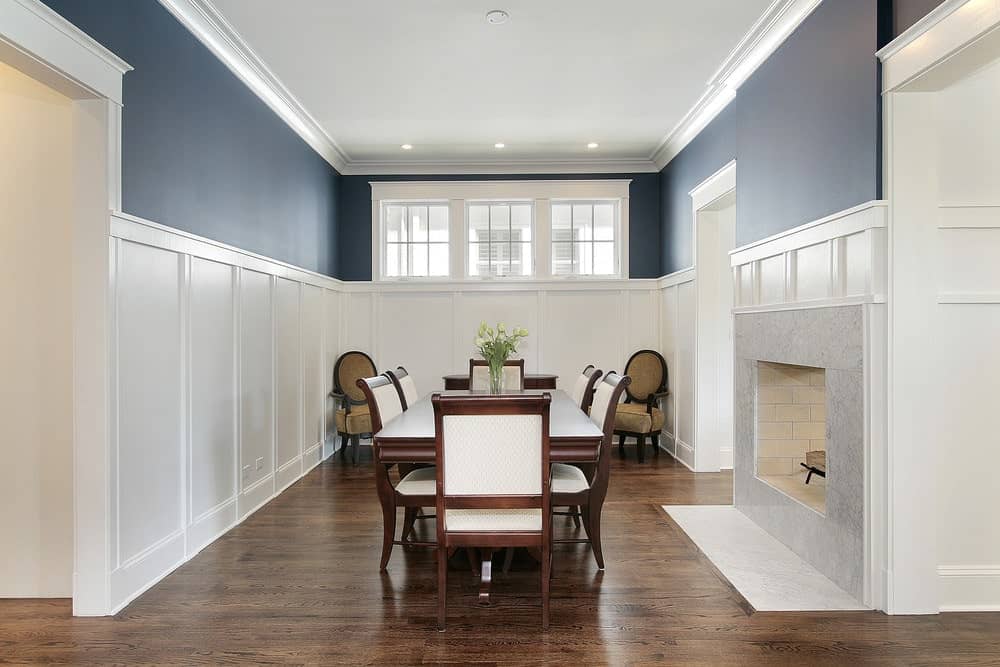墙饰的工艺为这个狭窄的房间带来了某种优雅。高高的落地窗打破了上层墙壁明亮的蓝色，加强了这一点。餐桌的中心是大理石壁炉，旁边是深色的木桌和椅子。