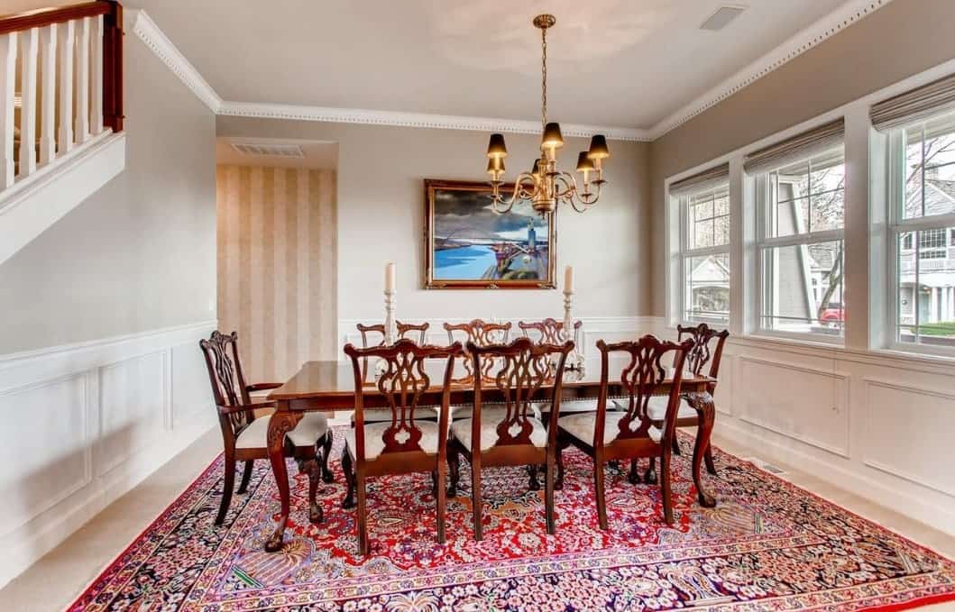 彩色图案的地毯主导着这个工匠风格餐厅的大理石地板，与被喜来登靠背椅子环绕的深色木质餐桌形成了鲜明的对比。优雅的吊灯与白色的墙壁和天花板相得益彰。