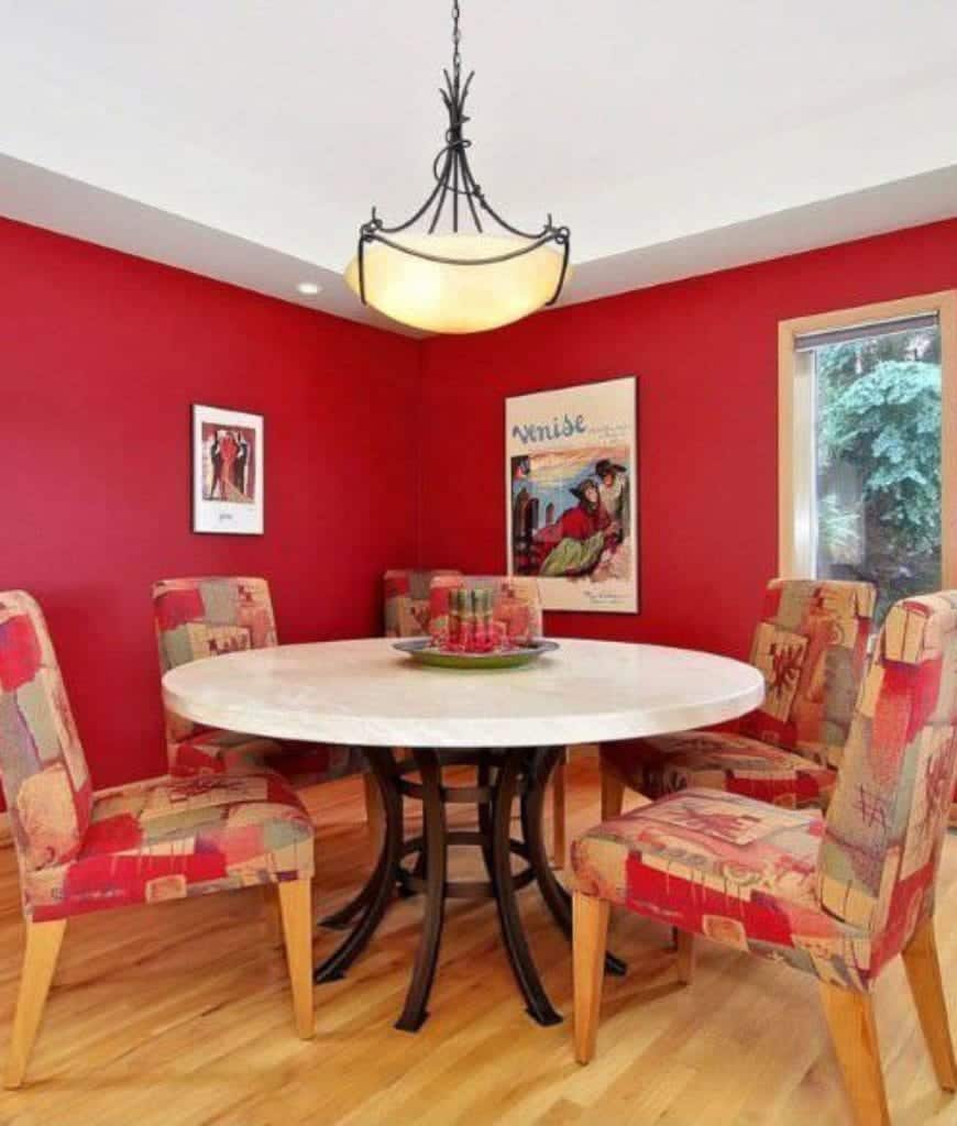 充满活力的红色色调主导着这个工匠风格的餐厅，鲜明的红色和红色图案的餐椅垫围绕着带有深色铁腿的白色圆桌。复古的壁挂式艺术品映衬着红墙和白色天花板。