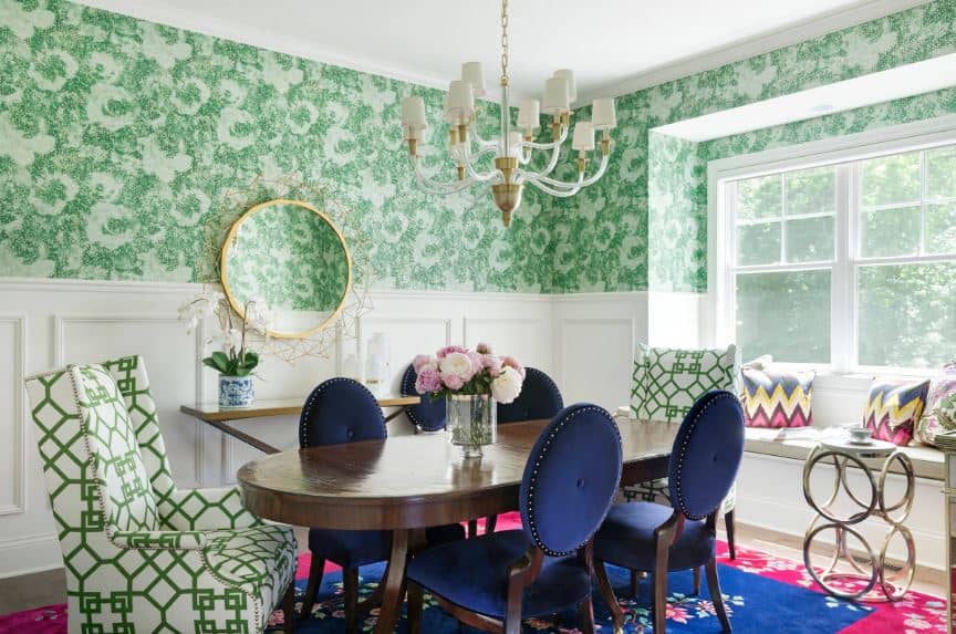 别致的绿色花卉墙有白色的护墙板，突出了深色木质餐桌和蓝色椭圆形靠背软垫椅。