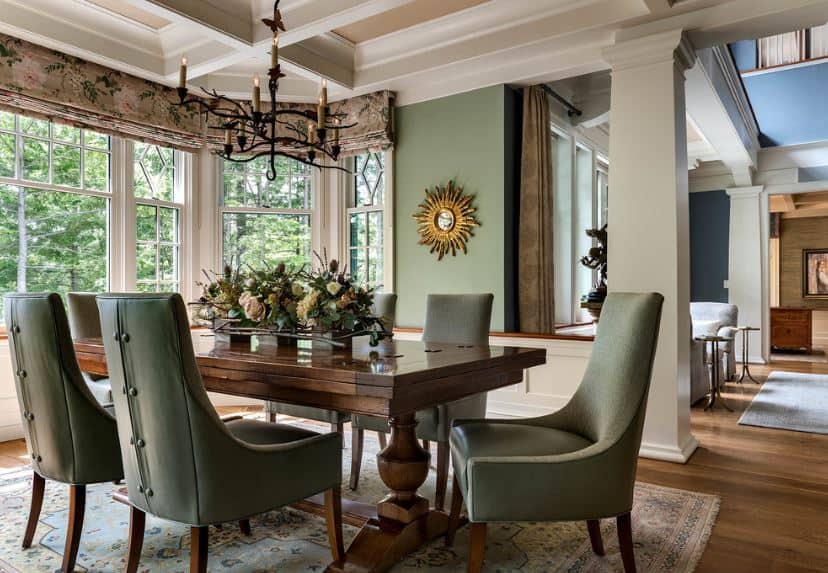 优雅的木桌周围的餐椅配有皮革靠垫，与绿色墙壁相呼应，与白色方格天花板和黑色铁吊灯形成对比。