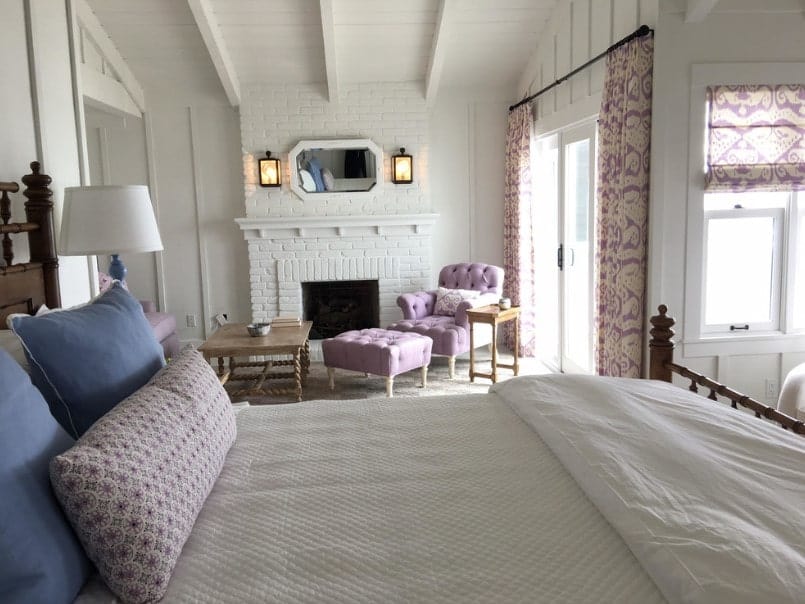 主卧室有一张舒适的大床和一张舒适的椅子，靠近砖壁炉的脚凳。