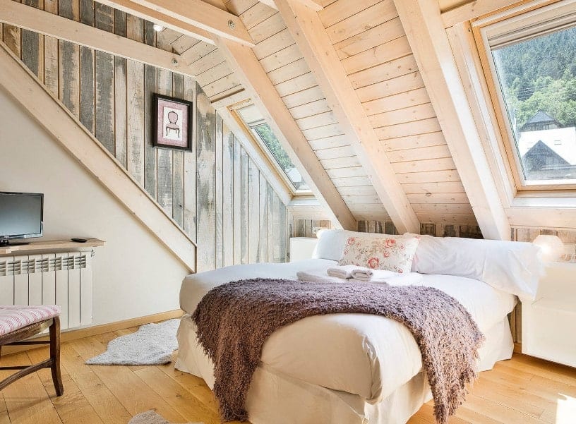 主卧室里舒适的白色床被木墙和天花板包围，还有硬木地板。
