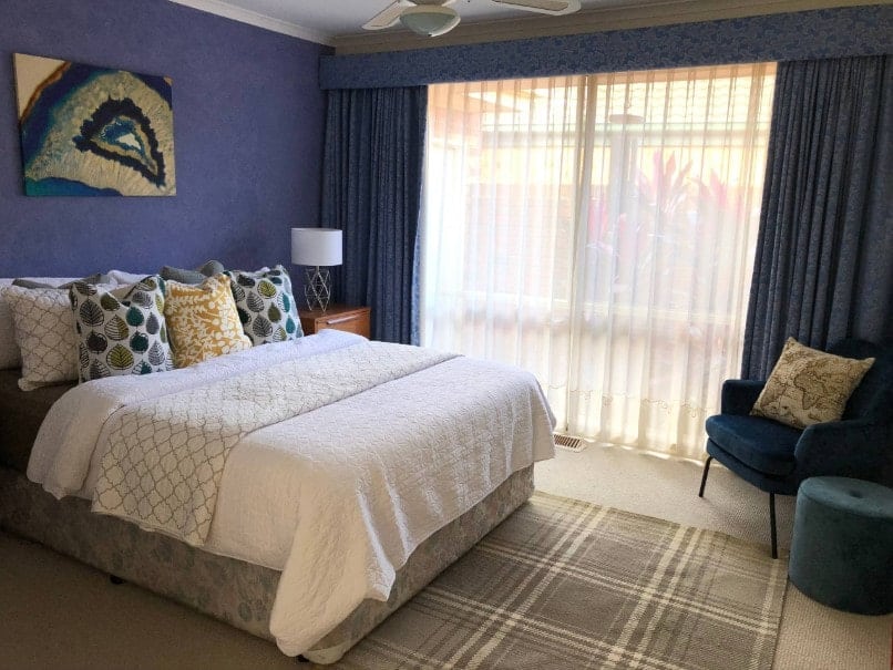 主卧室的蓝色墙壁与蓝色窗帘相匹配。房间提供了一个时尚和舒适的床由台灯照明。