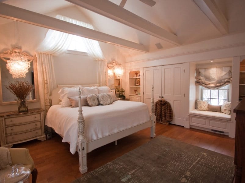 这间主卧室设有带裸露横梁的拱形天花板，以及硬木地板。床上有两个床头柜，由华丽的天花板灯照亮。