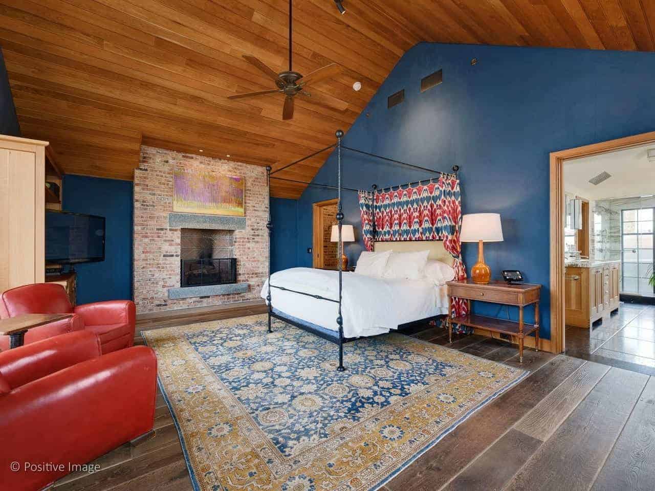 这间工业风格的主卧有一座镶有红砖的传统壁炉。这个房间在蓝色墙壁的映衬下显得格外突出，但与大教堂的木质天花板相得益彰，在四柱床上方有一个吊扇。